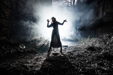 Naklejka premium A young witch dances and conjures on Halloween night in smoke and light at the festival of the dead.