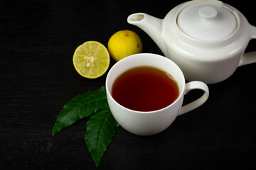 Neem tea in ceramic cup with neem leaf and lemon on black wooden background dark tone.
