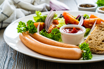 Breakfast - boiled sausages, bread and fresh vegetables served on wooden table

