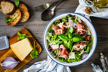 Tasty salad - prosciutto di Parma, parmesan and fresh, green vegetables on wooden table
