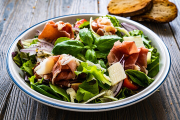 Tasty salad - prosciutto di Parma, parmesan and fresh, green vegetables on wooden table
