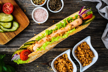 Hot dog - baguette with sausage and fresh vegetables on wooden table