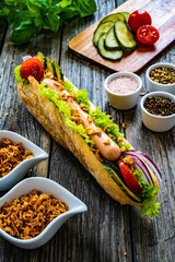 Hot dog - baguette with sausage and fresh vegetables on wooden table