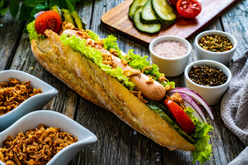 Hot dog - baguette with sausage and fresh vegetables on wooden table