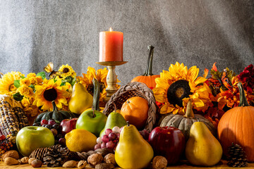Thanksgiving cornucopia overflowing with fruit nuts pumpkins sunflowers and burning candle