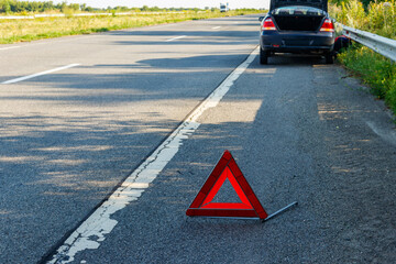 Red emergency stop sign (red triangle warning sign) and broken car on road