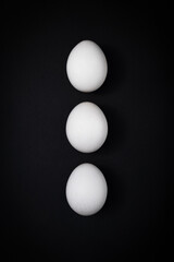 Breakfast triple: three white chicken eggs against a dark slate background. Table top view, flat lay, copy space.