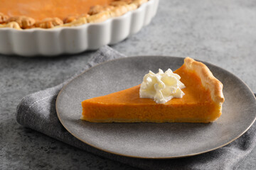 Piece of Traditional American Pumpkin Pie in plate on gray stone background. Close up. Homemade pastry for Thanksgiving Day.