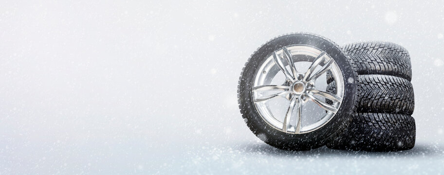 a set of winter tires and alloy wheels on a snowy white background. driving safety in winter and seasonal tire change in icy conditions