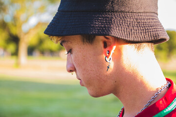 Portrait of a cool young Argentine man with earrings and a piercing wearing a bucket hat outdoors
