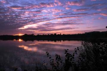 Purple and pink landscape of sunrise or sunset over a lake. Reflection of the clouds in the water. Symmetry of a dramatic sky.