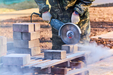 A worker with a circular saw cuts paving slabs in close-up.