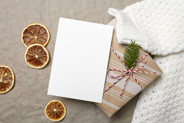 Fototapeta na wymiar Christmas greeting card mockup with decorated gift box, knitted sweater and dry oranges