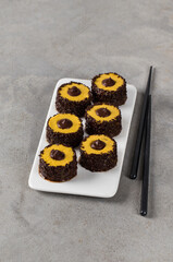 Sweet creamy pumpkin sushi rolls with chocolate sprinkles and filling on a ceramic plate on a light gray background 