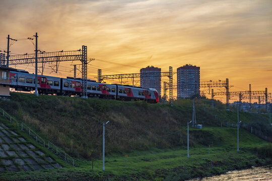 The high-speed electric train Lastochka of Russian Railways moves along a rampart against the backdrop of a picturesque sunset. Moscow, Russia