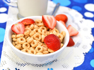 White bowl full of honey corn flakes rings and strawberry - breakfast on blue background