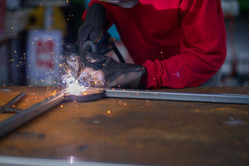 A male worker wearing protective clothing and gloves is welding steel with an electric welding machine.