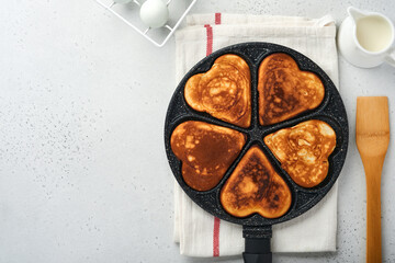 Pancakes in shape hearts with chocolate sauce in gray ceramic plate, cup of coffee on gray concrete background. Table setting for your favorite Valentines Day breakfast. Top view copy space.