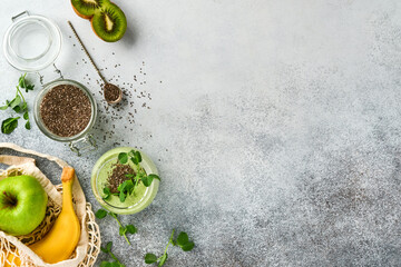 Ingredients for green smoothie, fresh organic spinach pea microgreens, banana, kiwi, apple and chia seed over light grey concrete background. Healthy eating ingredients. Top view, copy space