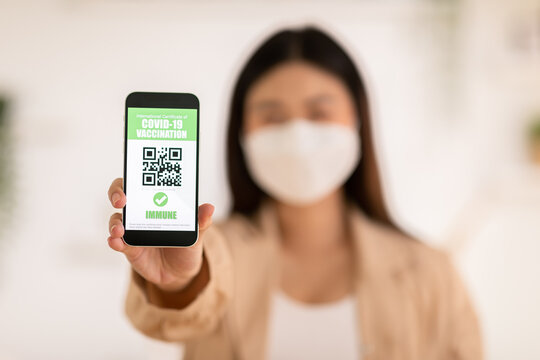 close up hand of woman holding and show COVID-19 vaccination passport on mobile phone.Safety woman wear face mask open app QR Code showing vaccination passport after received anti virus vaccine