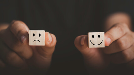 Customer service evaluation and satisfaction survey concepts. face smiley face icon on wooden cube, Hand holding two wooden cube happy face and Unhappy face.