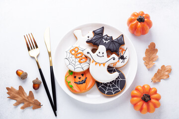 Halloween table setting with gingerbread cookies on white plate and cuterly on white background. Bright homemade cookies for Halloween party