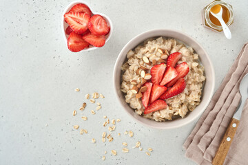 Oatmeal porridge with strawberry slices, nuts almonds and honey in blue bowl on grey table. Healthy eating, dieting, vegetarian food concept. Place for text