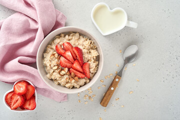 Oatmeal porridge with strawberry slices, nuts almonds and honey in blue bowl on grey table. Healthy eating, dieting, vegetarian food concept. Place for text
