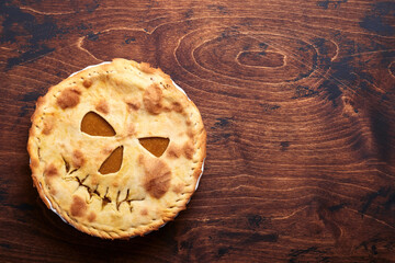 Halloween food. Homemade pumpkin pie or tart with a scary face for Halloween on a wooden table....