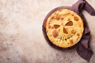 Halloween food. Homemade pumpkin pie or tart with a scary face for Halloween on a wooden table. Copy space. Halloween food concept.