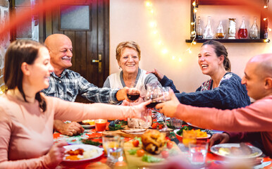 People toasting red wine and having fun at winter holidays reunion - Dinner celebration concept with happy adult friends sharing time together at home party - Warm filter with focus on central woman