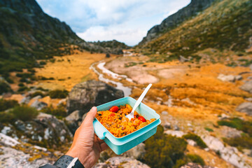 Man's hand holding plastic food container with healthy homemade food. Lunch while hiking in the...