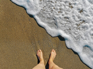 Bare feet and sea foam on a sandy beach. Top view