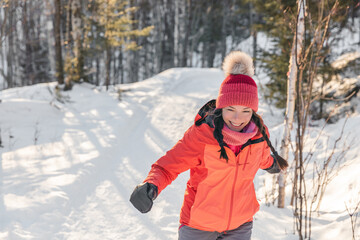 Fototapeta na wymiar Happy Asian woman laughing walking in snow forest during winter. Beautiful portrait of young adult smiling wearing cold weather hat and gloves, orange jacket