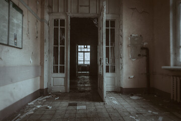 Obraz premium A dark corridor with a wooden door in an abandoned hospital. Terrible shabby walls. Beautiful old architecture of an abandoned building.