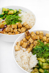Two vegan asian style bowls with fried tofu, rice, cucumbers, nut sauce seaweed and vegetables. Food sticks. Isolated on white, close up view.