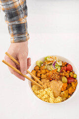 Vegan bowl with couscous, fried tofu, chickpeas, vegetables and peanut sauce, mans hand with food...