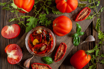 Dried tomatoes in a glass jar with olive oil with garlic and spices. Home canning, dehydration. Close-up, top view on vintage wooden background