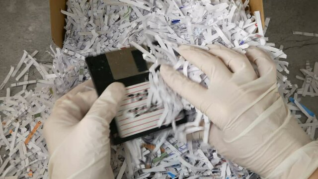 Top secret information on retro vintage floppy disk magnetic computer among shredder paper, thief information concept, closeup