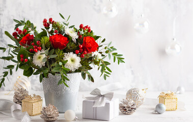 Festive winter flower arrangement with red roses, white chrysanthemum and berries in vase on table....