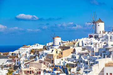 Greece vacation iconic background. Famous Oia village with traditional white houses and windmills during summer sunny day Santorini island, Greece.