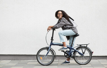 Young beautiful woman on bike over white wall background in a city, Smiling student girl with...