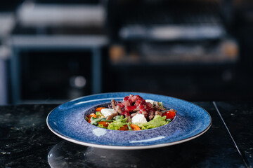 A professional chef serves a freshly prepared salad of tomato and veal greens with sauce in a gourmet restaurant close-up.