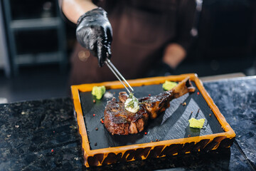 A professional chef beautifully serves a juicy grilled steak with butter and seasonings. Grilled meat in a restaurant.