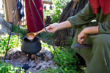 Hands that move the soup that is in a pot hanging over the fire. The pot is attached to a tripod....