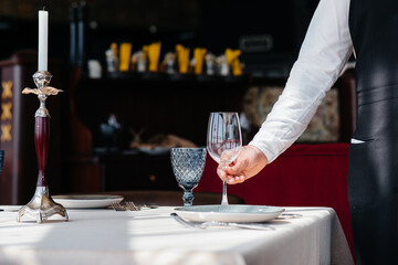 A young waiter in a stylish uniform is engaged in serving the table in a beautiful gourmet restaurant close-up. Restaurant activity, of the highest level.
