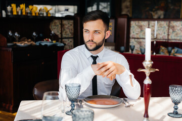 A young bearded male businessman is sitting at a table in a fine restaurant and waiting for his order. Customer service in the catering.