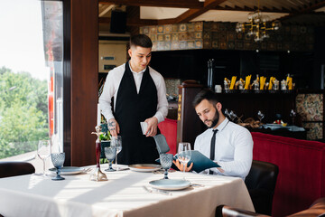 A young businessman in a fine restaurant examines the menu and makes an order to a young waiter in a stylish apron. Customer service.