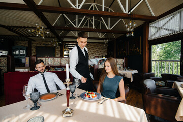 A stylish waiter serves a young couple who came on a date in a gourmet restaurant. Customer service in the catering.