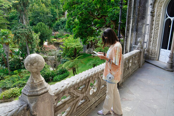 Fototapeta premium Young girl with a black mask and a camera on her wrist looking at a map outside the Regaleira Palace in Sintra (Portugal)